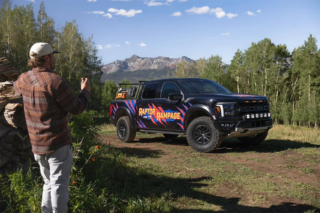 Man standing next to Raptor Rampage prize vehicle eating a SNICKERS® candy bar